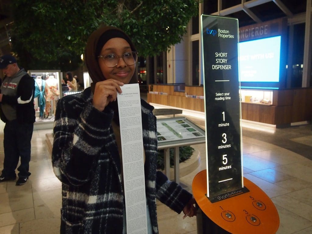 Yasmin shows off her story next to the short story machine in the Prudential Center