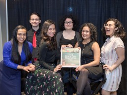 TiP staff and students sit at directors chairs holding a copt of the Teens in Print newspaper