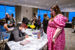 Smiling guest looks down at Neema Avashia autographing her book
