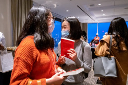 Two masked guests holding books laugh and look at each other