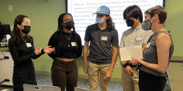 Group of students stand before a projector talking to each other