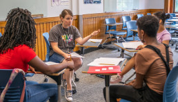 Youth participants and adult facilitator sit at desks in a circle