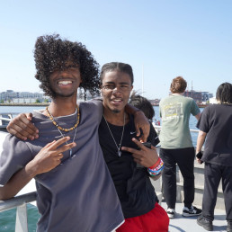 two students arm in arm, standing on the deck of a ferry in Boston Harbor