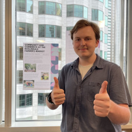 Student holds two thumbs up in front of an article printed on a poster