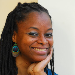 headshot of Zahra smiling and wearing a peacock feather earring