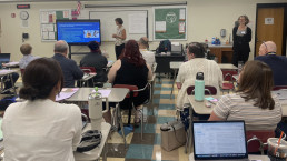A classroom of adults face forward to two instructors